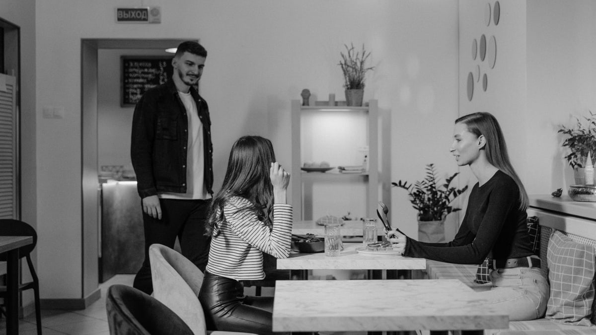A black and white scene of three adults socializing in a stylish cafeteria setting.